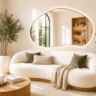 Bright organic living room with a curved boucle sofa, oversized asymmetrical mirror, natural wood accents, and large statement plants creating a cozy modern atmosphere.