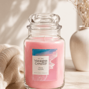 Elegant pink scented candle in a clear glass jar on a neutral beige background with soft natural lighting and minimal decor.