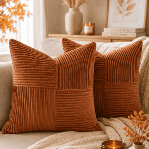 Rust-colored corduroy throw pillows on a cream sofa with pumpkin spice candle and cozy autumn home decor.