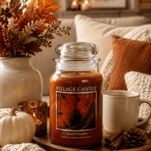 Pumpkin spice scented candle with autumn leaves, white pumpkin, cozy pillows, and warm fall living room decor.