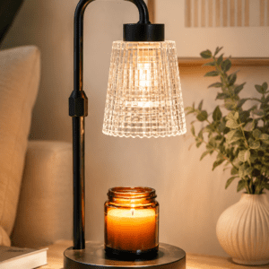 Modern black candle warmer lamp with a textured glass shade warming a scented candle on a wooden bedside table in a cozy living room.