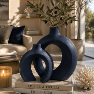 Modern navy blue ceramic vase set with olive branches displayed on decorative books in a stylish coastal living room.