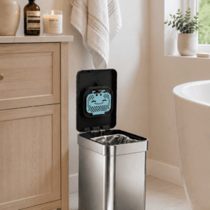 Modern stainless steel step trash can with soft-close lid placed beside a bathroom vanity in a bright, cozy, spa-inspired bathroom.