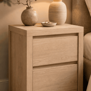 Modern light oak bedside table styled with a ceramic vase, table lamp, and minimalist accessories in a warm neutral bedroom.