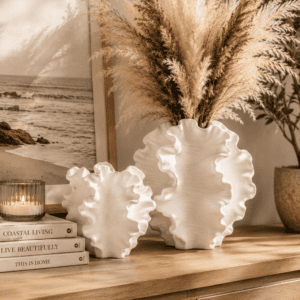 White sculptural ceramic vase set with dried pampas grass styled on a wooden console table with candles, framed artwork, and cozy neutral home decor.
