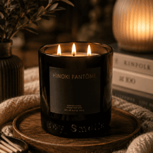 Luxury black glass triple wick Hinoki scented candle on a wooden tray with cozy knit blanket, books, and warm ambient lighting in a modern living room.
