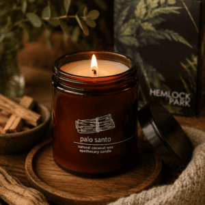 Luxury Palo Santo natural coconut wax candle in an amber apothecary glass jar on a wooden tray with rustic wood accents and cozy home decor.