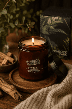 Luxury Palo Santo natural coconut wax candle in an amber apothecary glass jar on a wooden tray with rustic wood accents and cozy home decor.