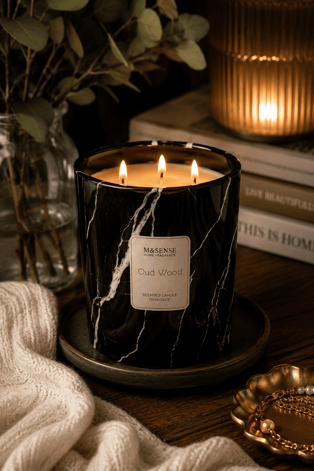Luxury black marble triple wick Oud Wood scented candle on a decorative tray with cozy knit blanket, books, and elegant home decor in a warm living room.