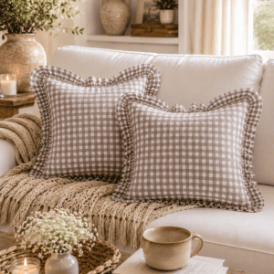 Taupe gingham ruffle throw pillow covers styled on a white sofa with a knitted throw, woven tray, candles, coffee mug, and warm farmhouse living room decor.