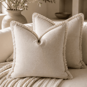 Natural linen fringe throw pillow covers on a cream sofa with a chunky knit blanket, olive tree, and warm neutral modern organic living room décor.