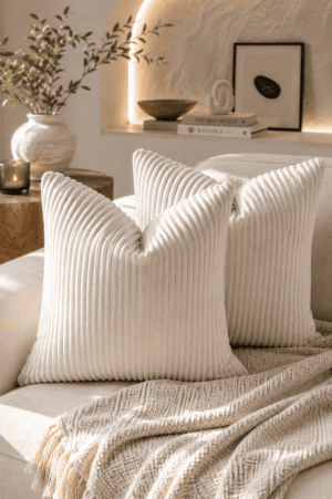 Ivory ribbed velvet throw pillow covers styled on a neutral sofa with a knitted throw blanket, candle, olive branches, and modern organic living room décor.
