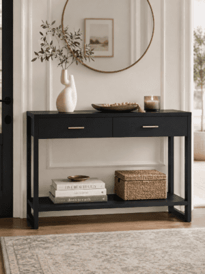 Black entryway console table with drawers, lower shelf, round mirror, ceramic vase, candle, decorative tray, books, and woven storage basket.
