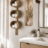 Woven bathroom towel wall organizer featuring three round natural fiber baskets filled with neatly rolled white towels, mounted vertically beside a light wood vanity in a warm neutral modern bathroom.