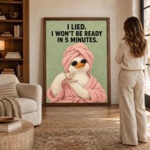 Framed funny duck print with pink bathrobe, towel, sunglasses, and getting ready quote, leaning against a wall beside a woman.